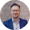 Professioneller Mann in Anzug lächelt vor neutralem Hintergrund, repräsentiert die Expertise von FactFinder im E-Commerce.